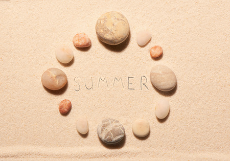 Round frame of sea stones with summer lettering drawn on sand. Summer beach background. View from aboveの写真素材