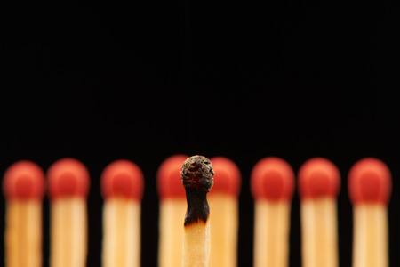 Burnt match standing in front of defocused set of eight red wooden matches, isolated on black backgroundの写真素材