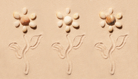Three flowers made of sea stones with stems and leaves drawn on sand. Summer beach background. View from aboveの写真素材