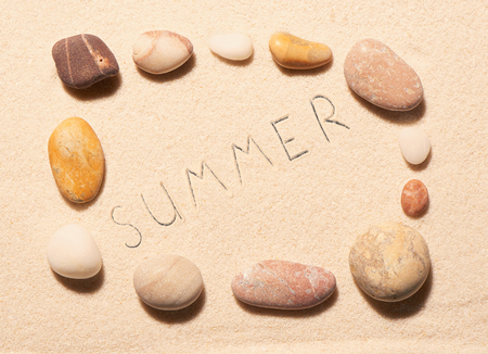 Rectangular frame of sea stones with summer lettering drawn on sand. Summer beach background. View from aboveの写真素材