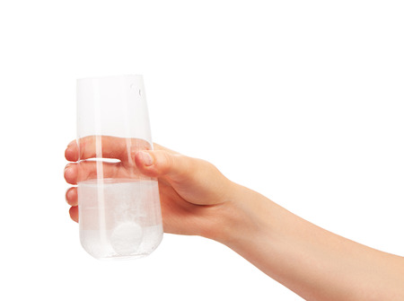 Close up of female hand holding clean transparent drinking glass with large white round effervescent tablet dissolving in water against white background.の写真素材