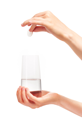 Close up of female hand holding large white round effervescent tablet over clean transparent drinking glass with water against white background.の写真素材