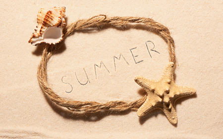 Oval frame of rope with starfish, empty sea shell and summer lettering drawn on sand. Summer beach background. View from aboveの写真素材