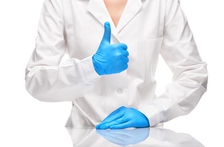 Close up of female doctor in white medical gown and blue sterilized surgical gloves showing thumbs up signの写真素材
