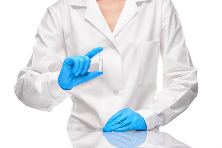 Close up of female doctor in white medical gown and blue sterilized surgical gloves holding transparent white glass ampoule with a drug against white backgroundの写真素材