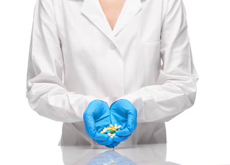 Close up of female doctor in white medical gown and blue sterilized surgical gloves holding pile of different tablets and capsules against white backgroundの写真素材