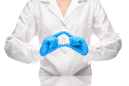 Close up of female doctor in white medical gown and blue sterilized surgical gloves holding transparent white glass ampoule with a drug against white backgroundの写真素材