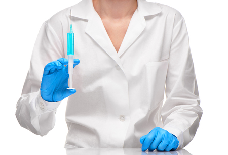 Close up of female doctor in white medical gown and blue sterilized surgical gloves holding with plastic medical syringe filled with blue drug against white backgroundの写真素材