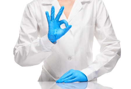 Close up of female doctor in white medical gown and blue sterilized surgical gloves showing OK signの写真素材