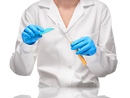 Close up of female in white gown and blue gloves holding two transparent white glass test tubes with yellow sorbent and blue liquid against white backgroundの写真素材