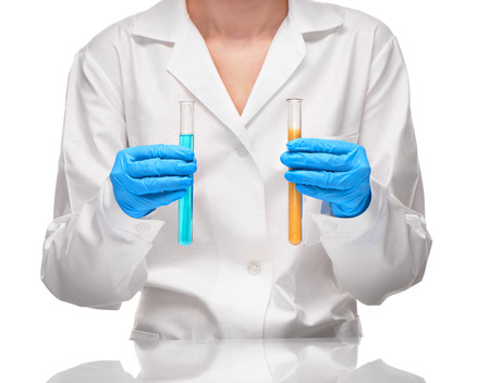 Close up of female in white gown and blue gloves holding two transparent white glass test tubes with yellow sorbent and blue liquid against white backgroundの写真素材