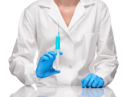 Close up of female doctor in white medical gown and blue sterilized surgical gloves holding plastic medical syringe filled with blue drug against white backgroundの写真素材