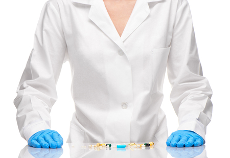 Pile of different tablets and capsules on table in front of female doctor in white medical gown and blue sterilized surgical gloves against white backgroundの写真素材