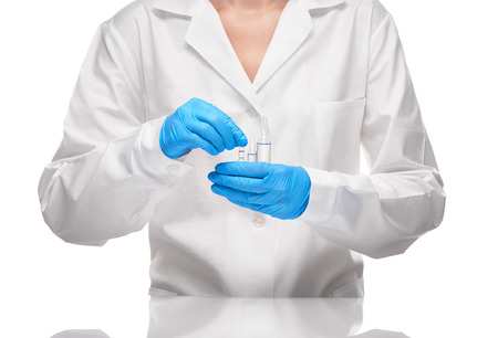 Close up of female doctor in white medical gown and blue sterilized surgical gloves holding three transparent white glass ampoules with drug against white backgroundの写真素材
