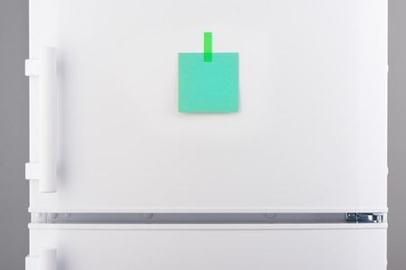 Blank green paper note attached with green sticker on white refrigerator doorの写真素材
