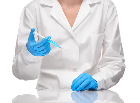 Close up of female doctor in white medical gown and blue sterilized surgical gloves holding plastic medical syringe filled with blue drug against white backgroundの写真素材