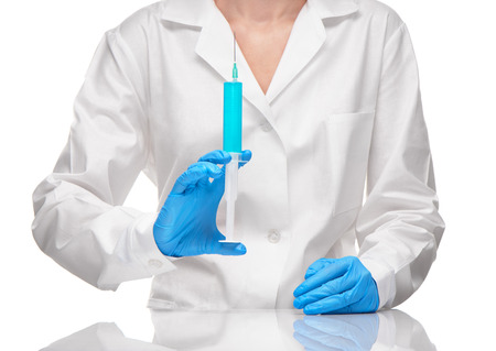 Close up of female doctor in white medical gown and blue sterilized surgical gloves holding plastic medical syringe filled with blue drug against white backgroundの写真素材