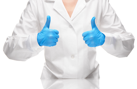 Close up of female doctor in white medical gown and blue sterilized surgical gloves showing thumbs up signsの写真素材