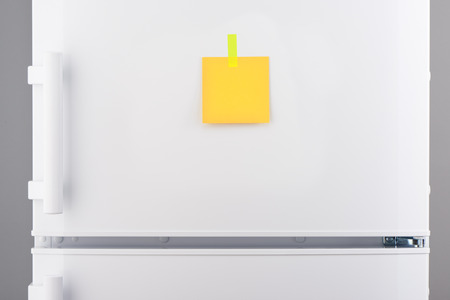 Blank yellow paper note attached with yellow sticker on white refrigerator doorの写真素材