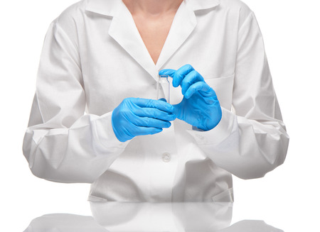 Close up of female doctor in white medical gown and blue sterilized surgical gloves holding empty transparent white glass ampoule against white backgroundの写真素材