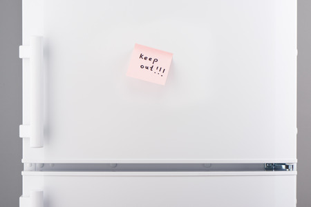 Keep out note on light pink sticky paper on white refrigerator doorの写真素材