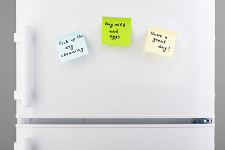 Pick up the dry cleaning, buy milk and eggs, have a great day notes on blue, green and yellow sticky paper on white refrigerator doorの写真素材