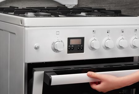 Female hand opening oven in white kitchen gas stove on gray backgroundの写真素材