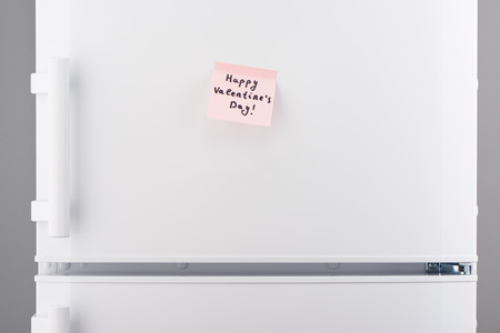 Happy valentines day note on light pink sticky paper on white refrigerator doorの写真素材