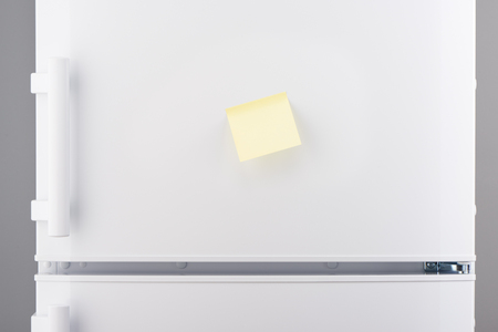 Blank light yellow sticky paper note on white refrigerator doorの写真素材
