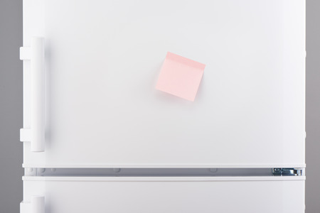 Blank light pink sticky paper note on white refrigerator doorの写真素材