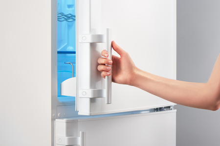 Female hand opening white refrigerator door on gray backgroundの写真素材