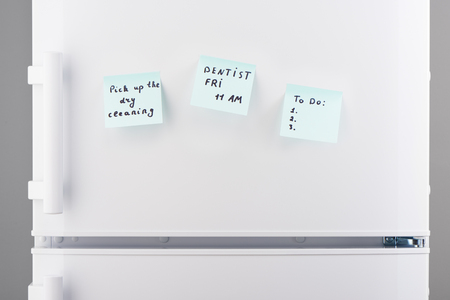 Pick up the dry cleaning, dentist friday 11 am notes and template for to do list on light blue sticky paper on white refrigerator doorの写真素材