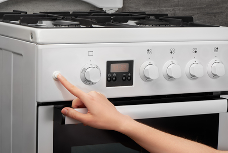 Female hand turning on white kitchen gas stove on gray backgroundの写真素材