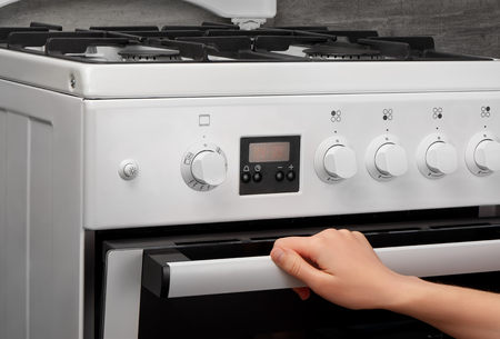 Female hand opening oven in white kitchen gas stove on gray backgroundの写真素材