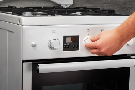 Male hand turning on white kitchen gas stove on gray backgroundの写真素材