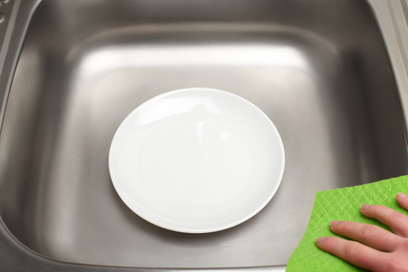 Close up of kitchen sink with clean white plate and green rag in female handの写真素材