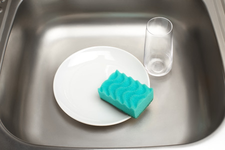 Close up of kitchen sink with clean white plate, green cleaning sponge and drinking glassの写真素材