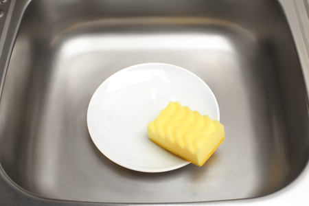 Close up of kitchen sink with clean white plate and yellow cleaning spongeの写真素材