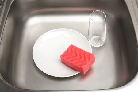 Close up of kitchen sink with clean white plate, pink cleaning sponge and drinking glassの写真素材