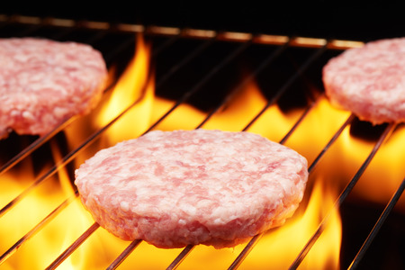 Raw hamburgers cooking on grill with flameの写真素材