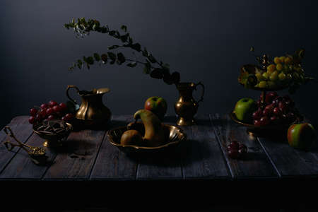 Fruit still life with grapes, apples, pears, chocolate and antique copper utensils on dark wooden table backgroundの写真素材