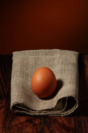 Brown chicken egg on burlap napkin on dark wooden table and warm rustic background