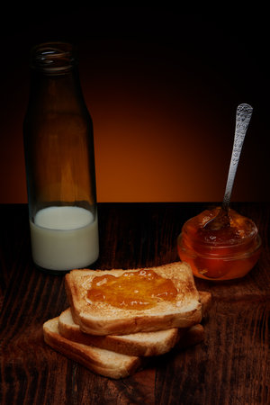 Crispy slices of toast with apple jam and bottle of milk on dark wooden table and warm rustic backgroundの写真素材