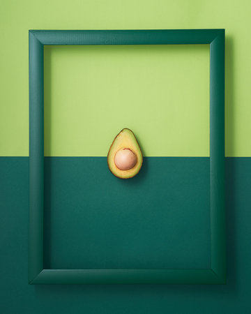 Cut in half avocado in wooden picture frame on two-tone green backgroundの写真素材