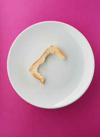 Leftover toast crust on white plate and bright pink backgroundの写真素材