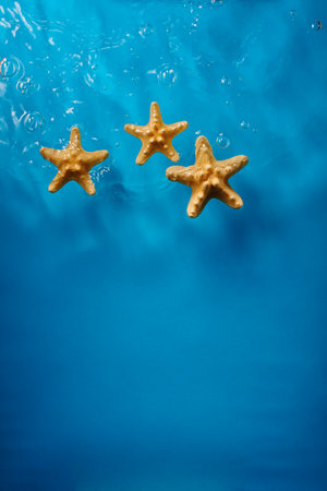 Three starfish in bright blue ocean water with waves and bubblesの写真素材