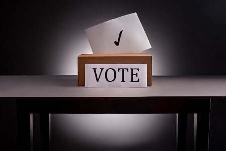 Ballot paper with tick sign sticks out of voting box on desk on gray background with dramatic lightingの写真素材