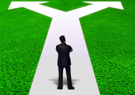 Business man standing on the white arrow on the green grass background.の写真素材