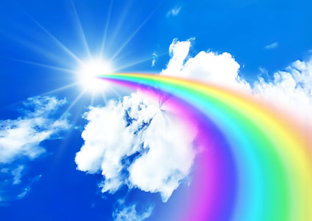 Rainbow in the blue sky with white clouds and sun rays.の写真素材