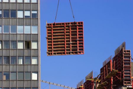 Tower crane lifting heavy red concrete frame